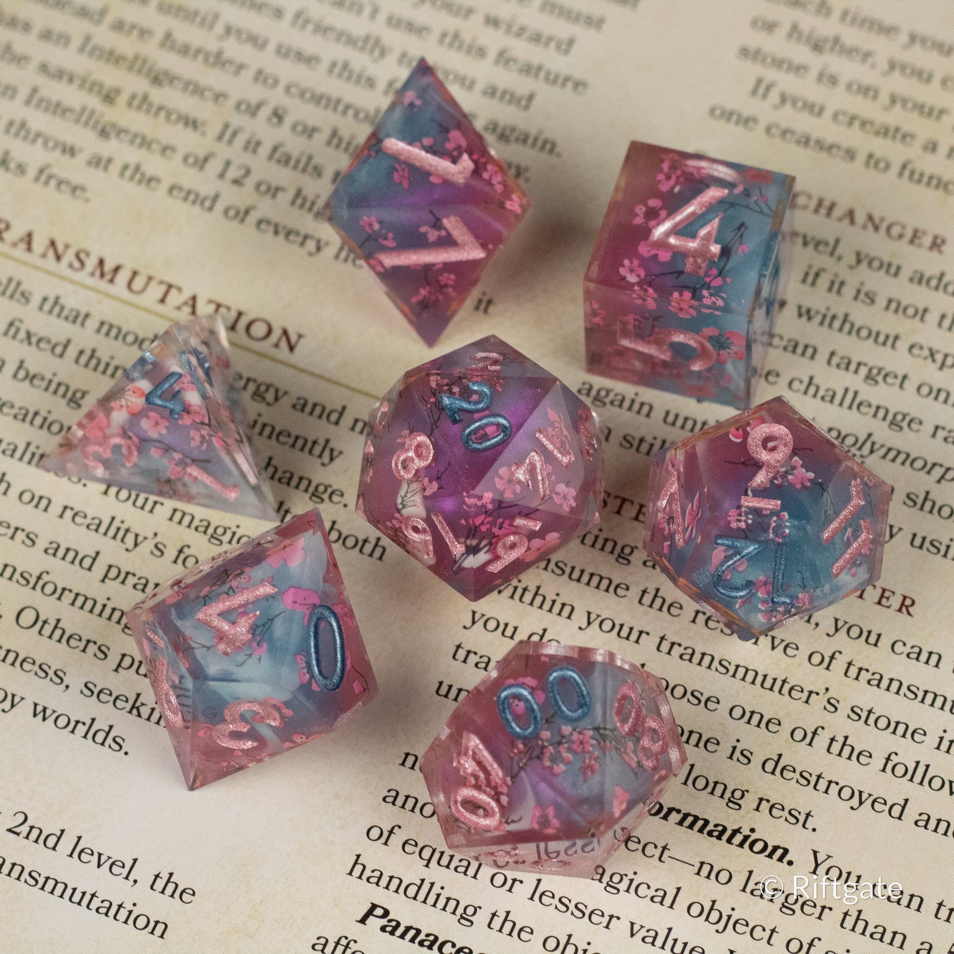 Twilight Blossoms Dice Set - Purple and pink sharp-edged polyhedral dice set with blue numbers and floral inclusions.