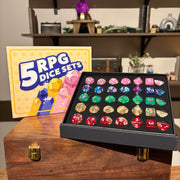5 RPG Dice Set Box - Colorful RPG dice set with five polyhedral shapes in a black display box, next to a yellow 5 RPG Dice Sets packaging box and