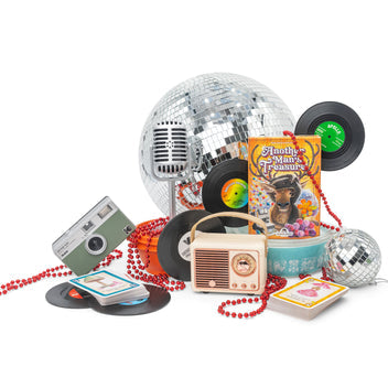 Another Man's Treasure - Retro card game box with vintage microphone, cassette player, vinyl records, disco balls, and red bead necklaces arranged.