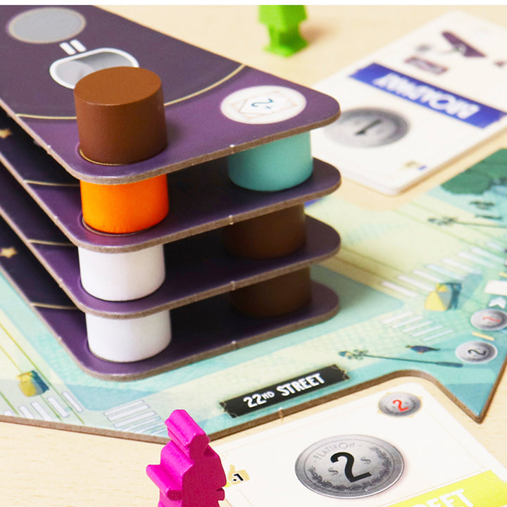 Flatiron - Stacked purple game tiles with multicolored wooden cylinders and a pink player token on a detailed game board.
