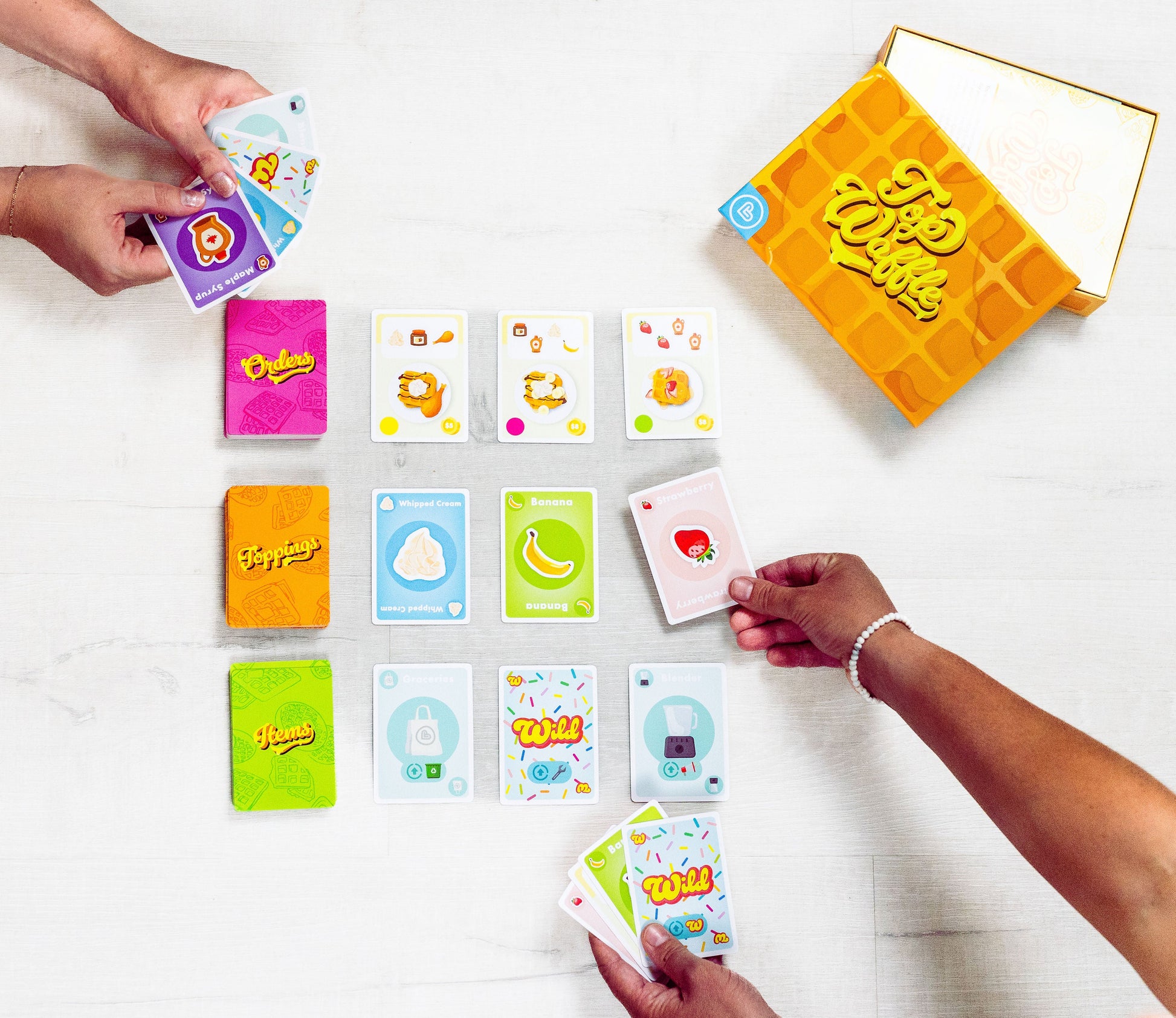 Top Waffle - Colorful rectangular playing cards with playful icons and text, arranged on a white surface, accompanied by a yellow.