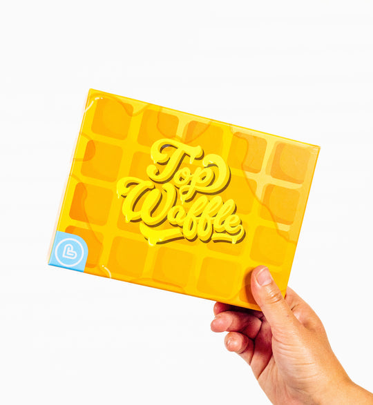 Top Waffle - Yellow waffle-patterned card game box with embossed "Top Waffle" text held by a hand.