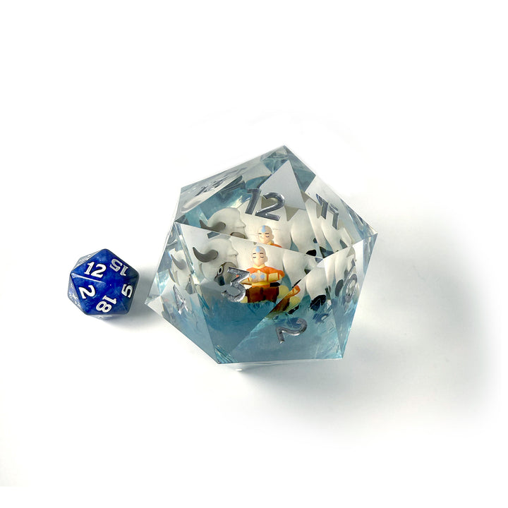 Sirius Dice 55mm Spindown d20: Magic the Gathering: Avatar The Last Airbender - Large transparent 20-sided dice with blue numbers and an Avatar The Last Airbender figure inside, shown next to a standard.