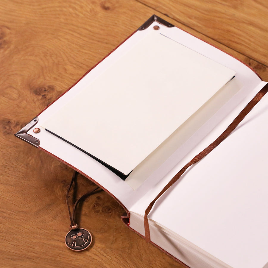 Critical Role Sketchbook - Brown leather-bound sketchbook with blank white pages and a black elastic strap, resting on a wooden surface.