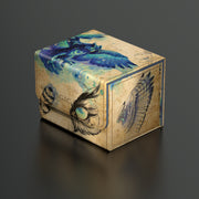 Ultimate Guard Sidewinder 100+ Deck Box: Bloomburrow - Maha, Its Featherless Night - Rectangular deck box with beige, blue, and black fantasy-themed artwork featuring a blue dragon and mystical feathers.