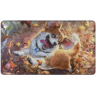 Playmat: Magic the Gathering: Modern Horizons 3: Phel, Exuberant Shepherd Holofoil. A holofoil play mat depicting Phel, a blue eyed blond and white corgi, flying through the air in delight on a breeze of autumn leaves with a small town blurred far below in the background.