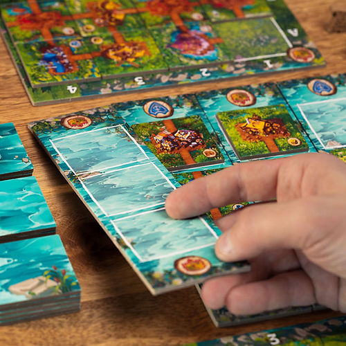 Timber Town - Hand holding a rectangular game tile with blue water and illustrated characters, next to other colorful game tiles on a.