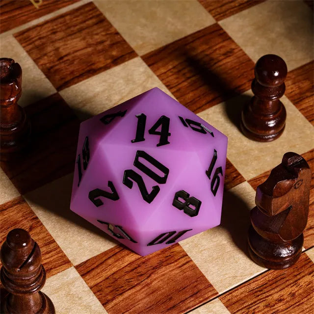 Giant Bouncy D20 - Glow In The Dark Purple - Large purple twenty-sided die with black numbers, glowing slightly, placed on a wooden chessboard among dark wooden chess.