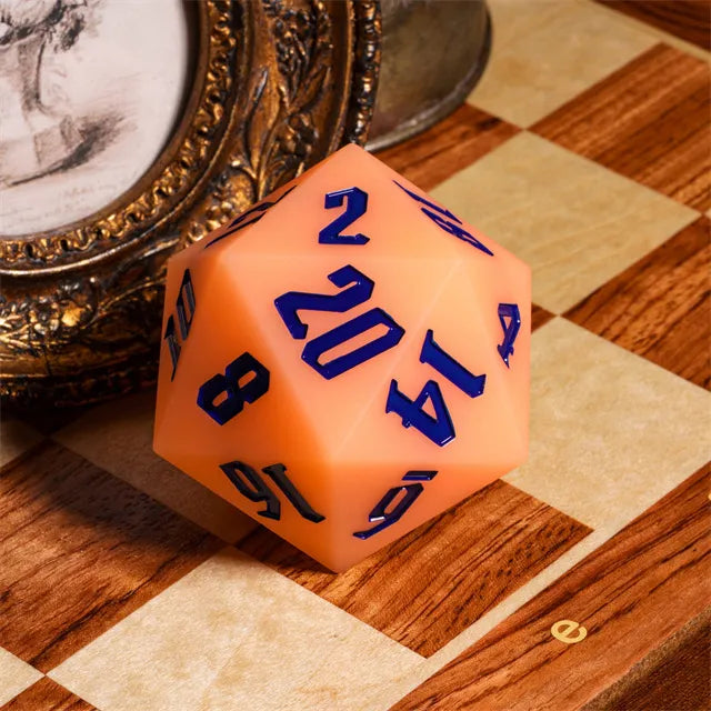 Giant Bouncy D20 - Glow In The Dark Orange - Large twenty-sided orange die with bold blue numbers, glowing in the dark, resting on a wooden chessboard.