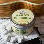 Bard's Blessing Gaming Candle - Round metal tin candle labeled Bard's Blessing with musical notes and natural wood surface background.