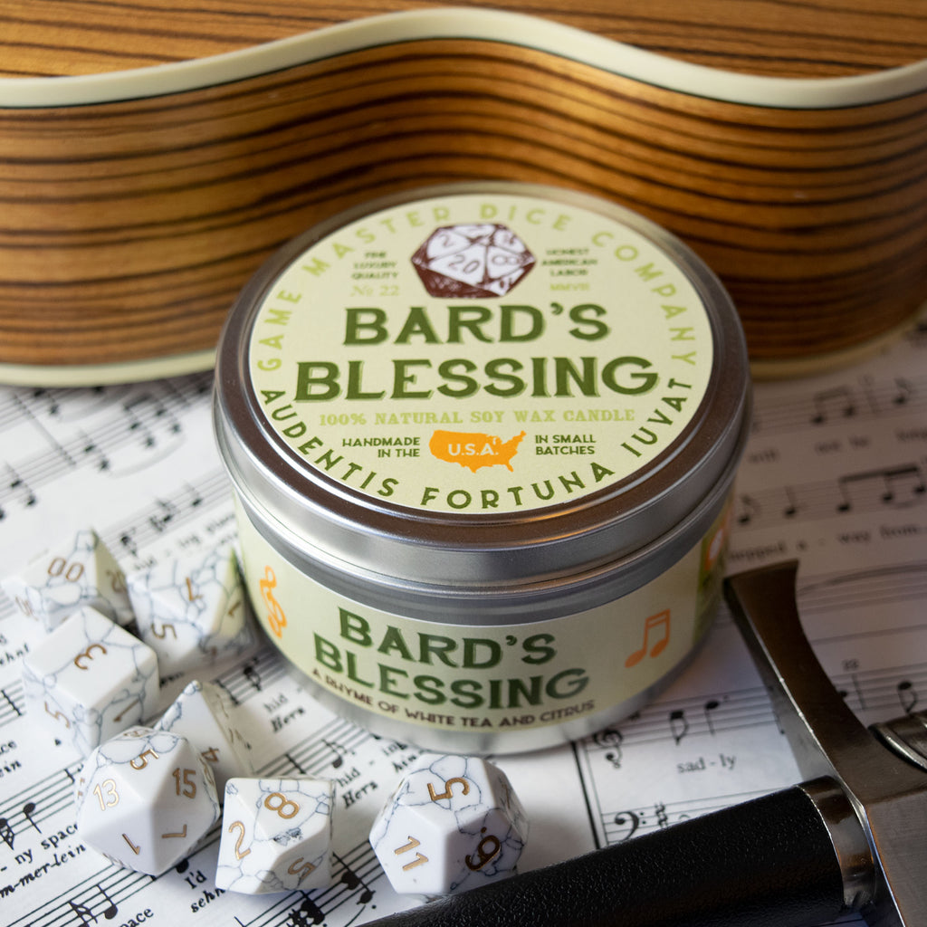 Bard's Blessing Gaming Candle - Round metal tin candle labeled Bard's Blessing with musical notes and natural wood surface background.