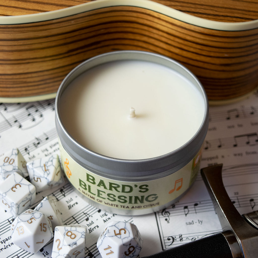 Bard's Blessing Gaming Candle - Round silver tin candle with white wax labeled Bard's Blessing, surrounded by white role-playing dice on sheet music.