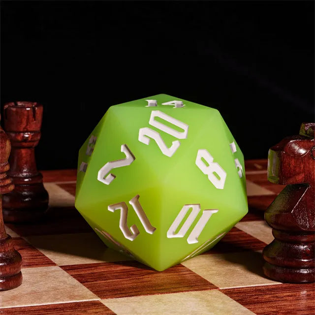 Giant Bouncy D20 - Glow In The Dark Green - Large green icosahedron-shaped die with white numbers, glowing surface, resting on a wooden chessboard.