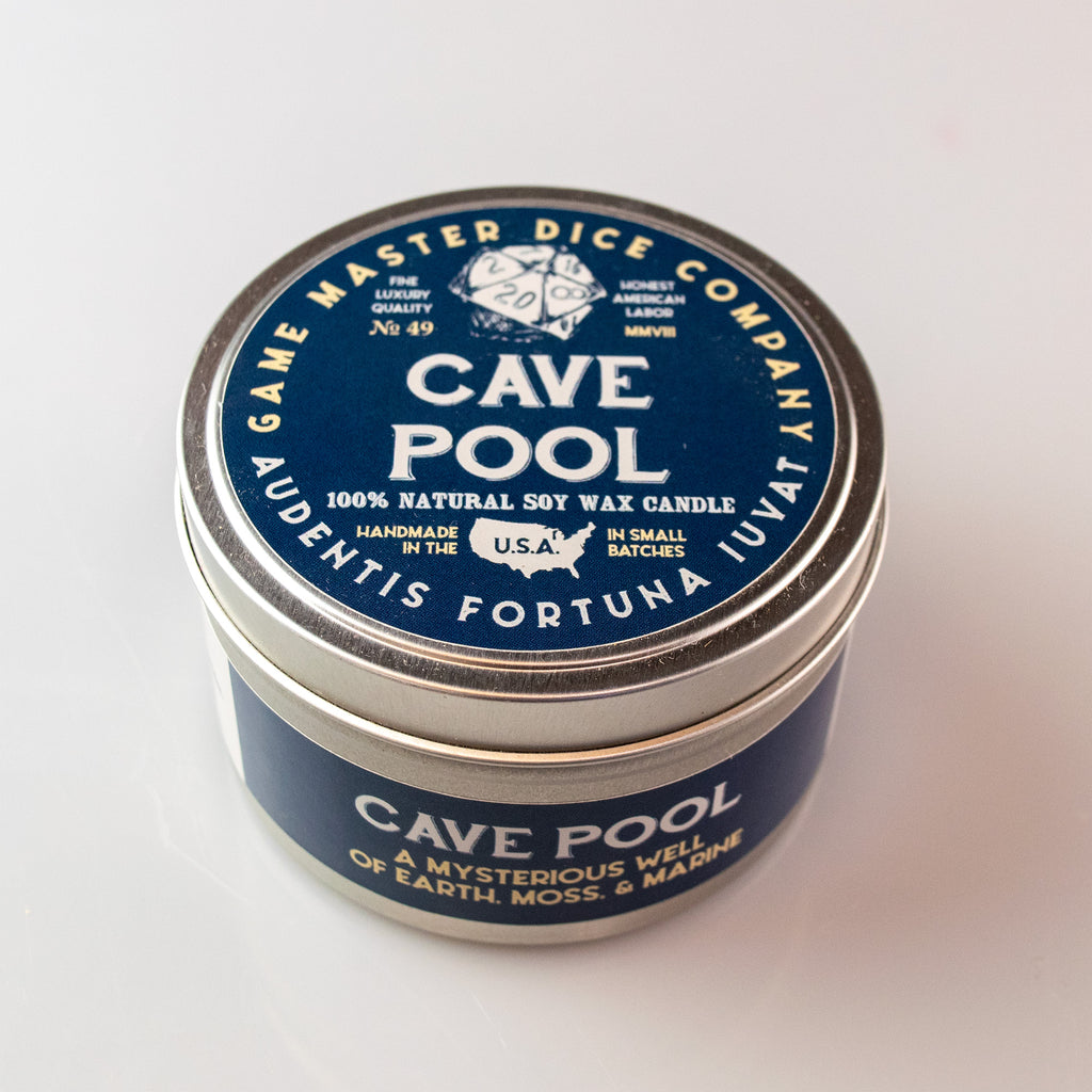 Cave Pool Gaming Candle - Round metal tin candle with navy blue label, white text, and logo featuring a 20-sided die design.