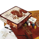 Tsuro: The Game of the Path - Tsuro board game box with dragon artwork, colorful game stones, rulebook, and cards on wooden surface.