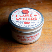 Cure Wounds Gaming Candle - Round metal tin candle with white label featuring red text and a red cross, labeled "Cure Wounds" with eucalyptus essential.