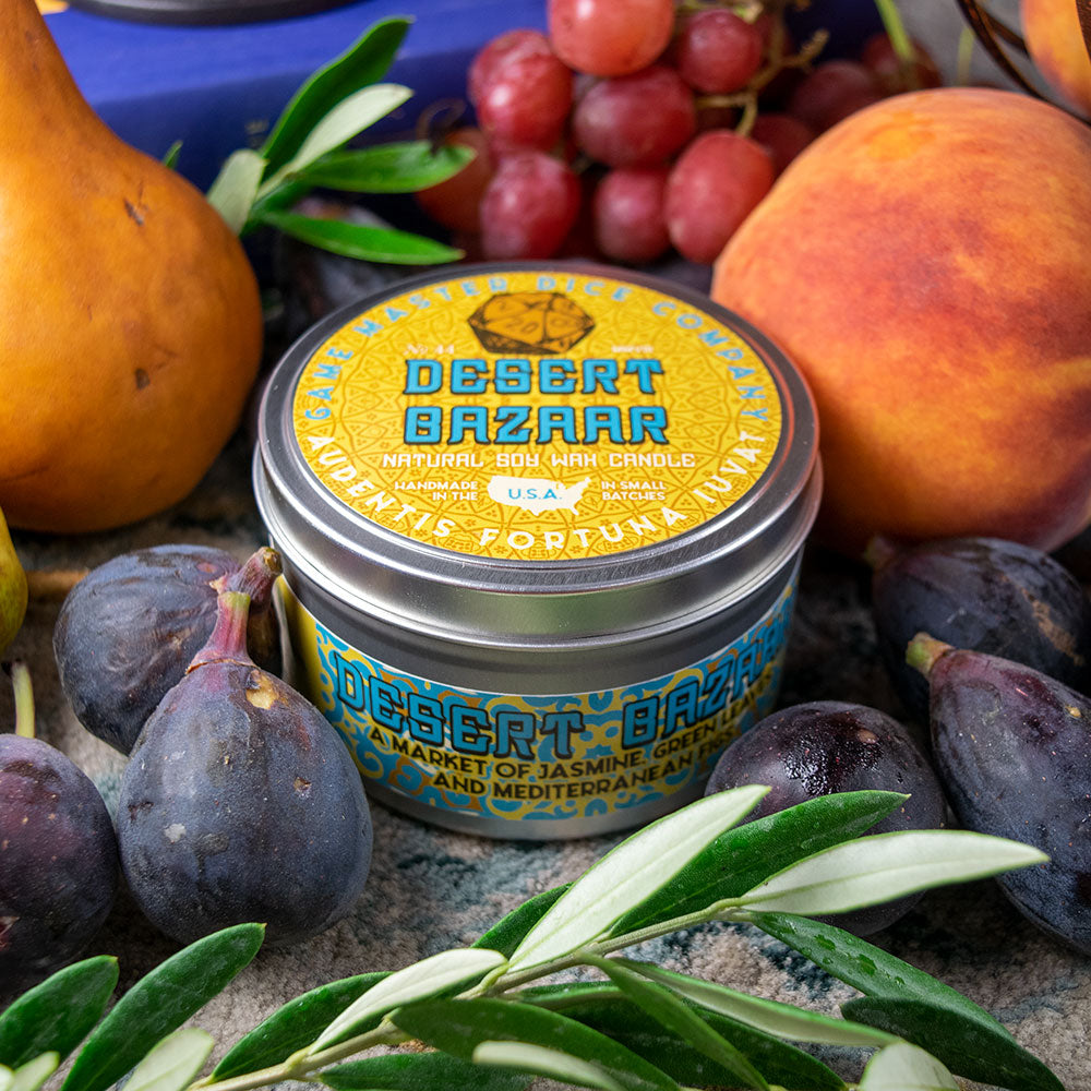 Desert Bazaar Candle - Small round metal tin candle with bright yellow and blue label reading Desert Bazaar, surrounded by fresh figs, grapes, a.