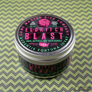 Eldritch Blast Gaming Candle - Round metal tin candle labeled Eldritch Blast with neon pink and green text on black lid, showing skull and rose graphics.