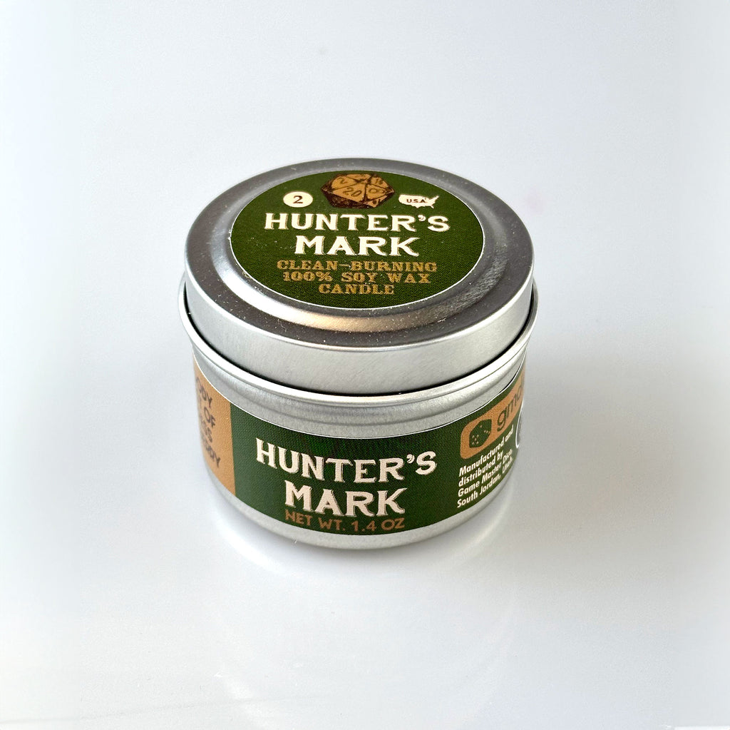 Hunter's Mark Gaming Candle - Small round metal tin with green and brown label reading "Hunter's Mark Gaming Candle" and "Woods and Leaves Scent".