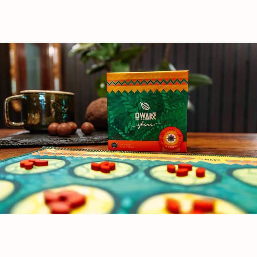 Ludos Africa Collection - Green and orange patterned Ludos Africa Collection game box on wooden table with circular game board and red tokens.
