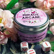 Mirage Arcane Gaming Candle - Round metal tin candle with pink label decorated with cherry blossoms and white dice around it.