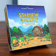 Stardew Valley: The Board Game - Square board game box featuring colorful pixel art farm scene with crops, barn, and characters under a bright blue sky with.