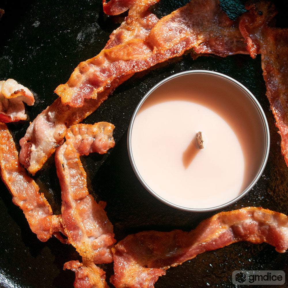 Second Breakfast Candle - Round white candle in metal tin surrounded by crispy cooked bacon strips on a black surface.