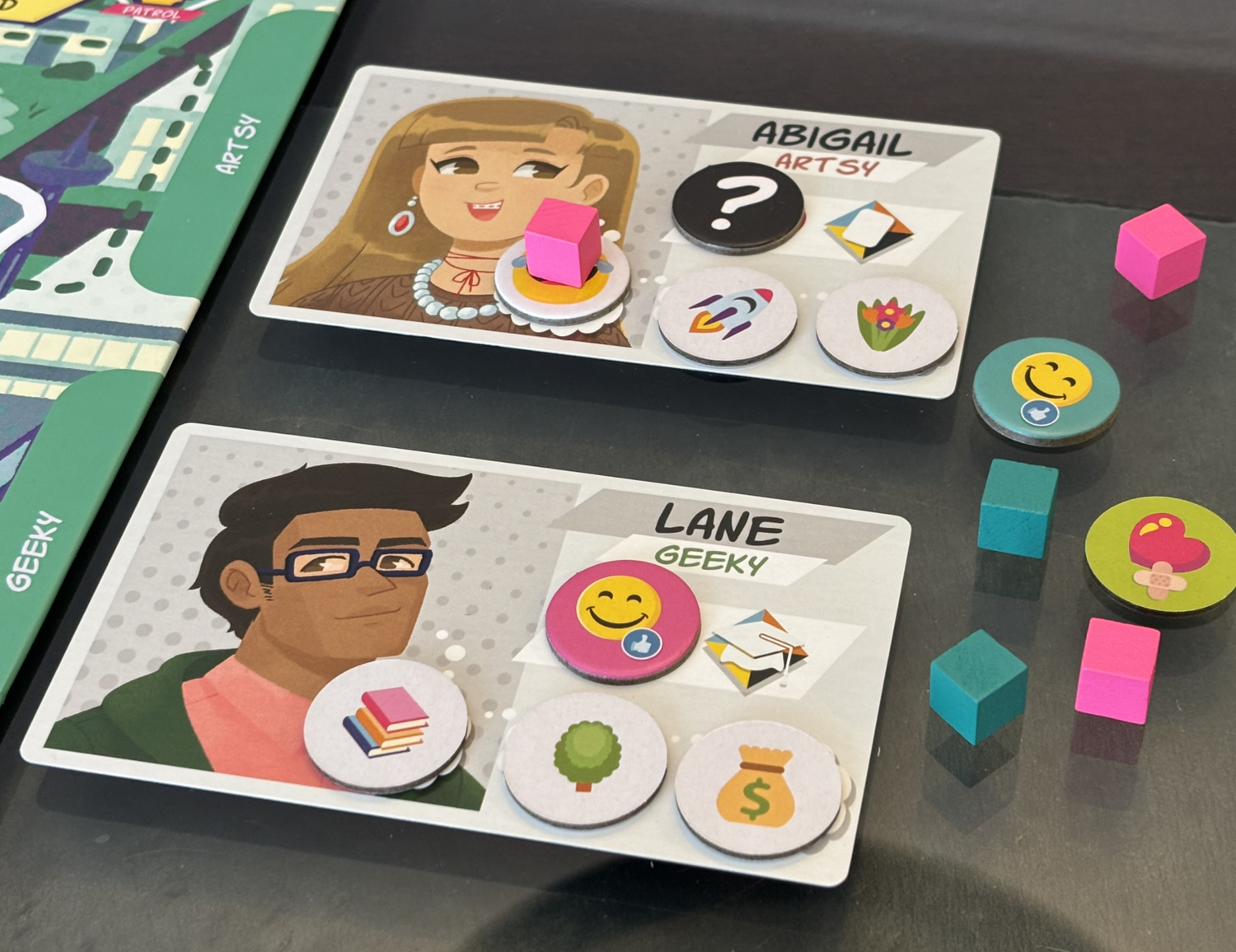 Super Squad High - Cards featuring illustrated characters Abigail and Lane with icons and colorful tokens on a game board surface.