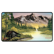 Playmat: Stitched Edge: Bob Ross: Mountain Retreat - Rectangular playmat with stitched black edges, featuring a painted mountain landscape, pine trees, a river, and a rustic.