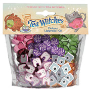 Tea Witches: Upgrade Kit - Clear bag with colorful game tokens including purple swirls, green leaves, white teeth, and gray eyes under Tea Witches.
