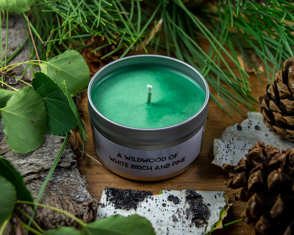 White Forest Gaming Candle - Green wax gaming candle in a gray metal tin labeled "A wildgoose of white birch and pine" surrounded by pinecones and.