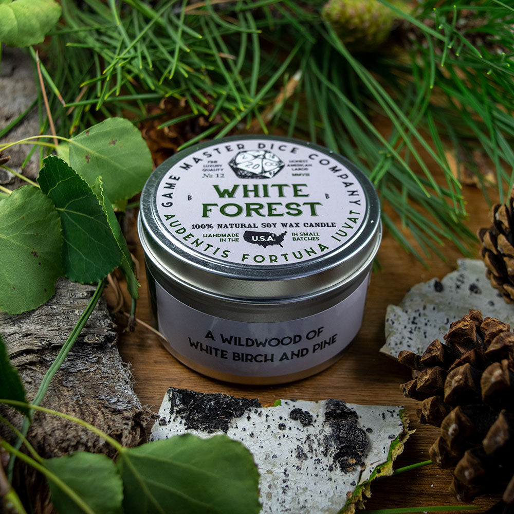 White Forest Gaming Candle - Round metal tin candle with white label featuring green forest illustration and text, placed on natural wood with green.