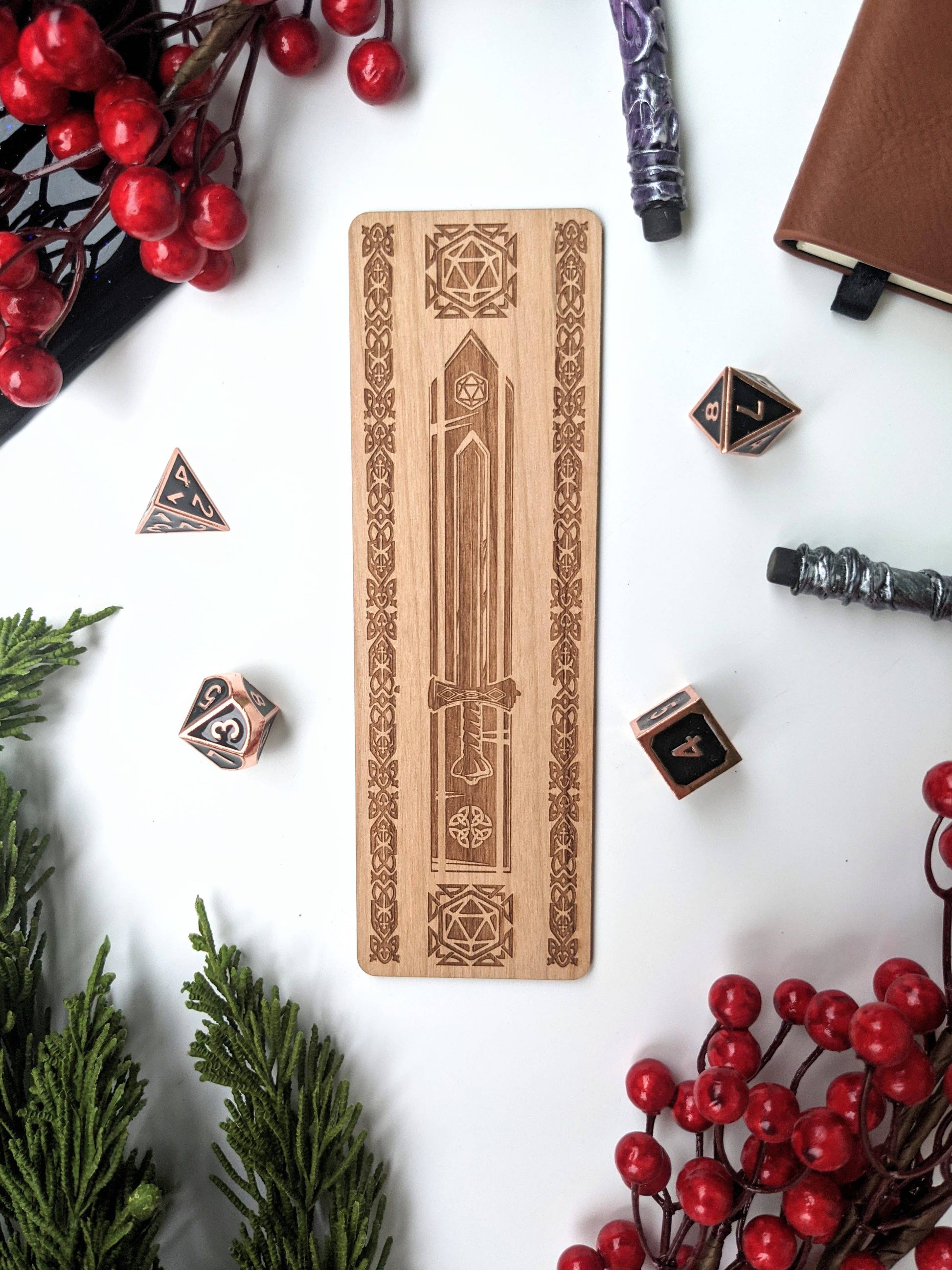 Celtic Dice Sword Bookmark - Wooden bookmark with engraved Celtic sword and decorative borders surrounded by black polyhedral dice and red berries.