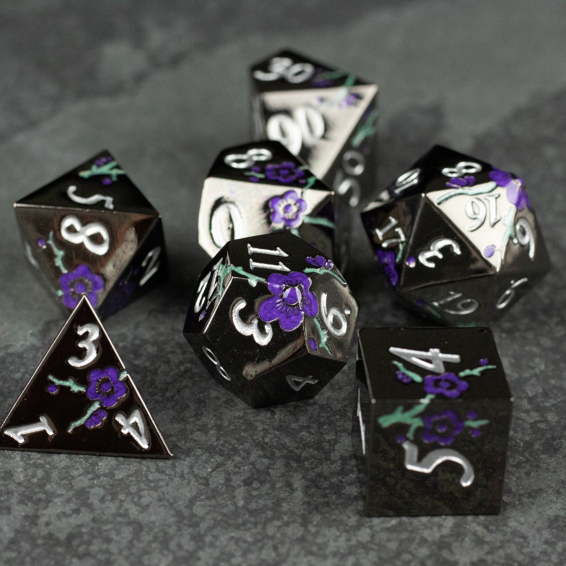 Black and Purple Metal Flower Dice - Set of black metal polyhedral dice with purple floral engravings and white numbering, including d4, d6, d8, d10, d12, and.