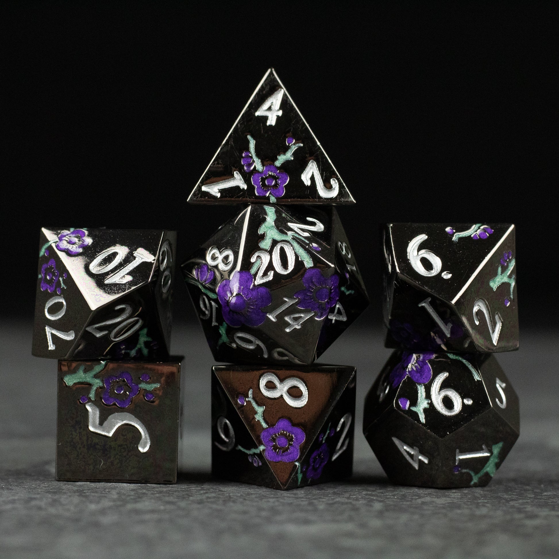 Black and Purple Metal Flower Dice - Set of seven black metal polyhedral dice with purple floral accents and white numbering for tabletop gaming.