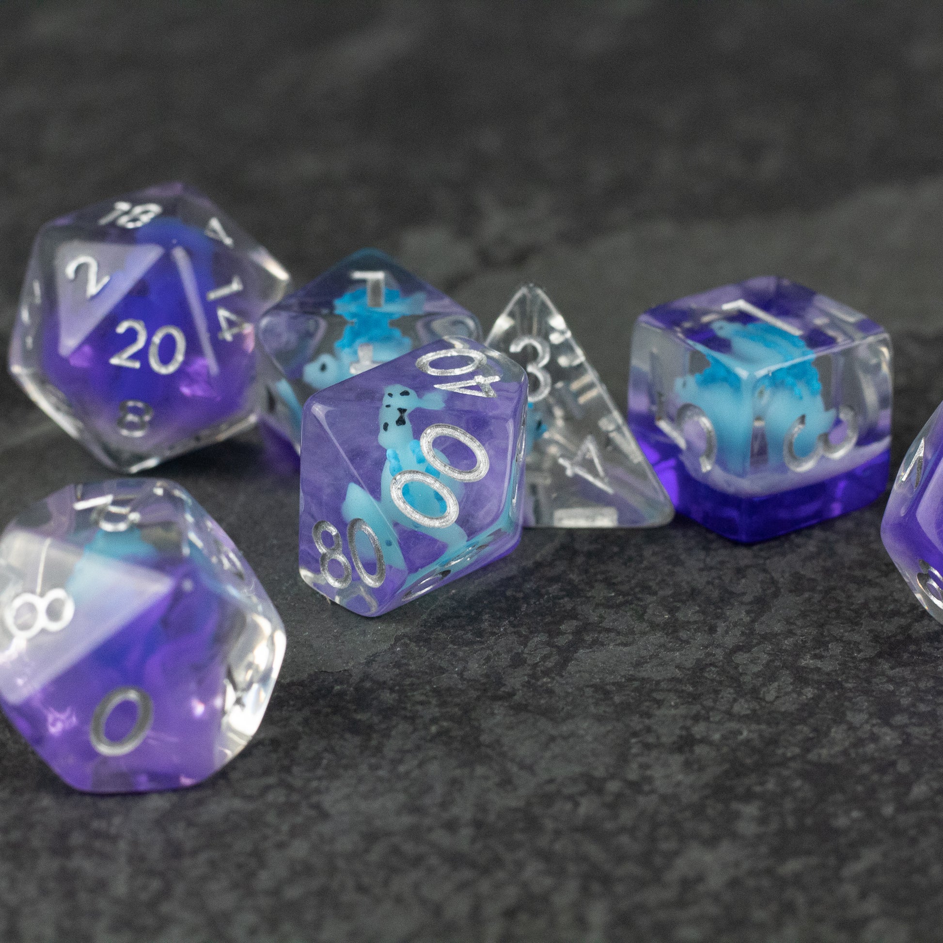 Blue Stegosaurus Dice Set - Set of seven translucent blue and purple polyhedral dice with white numbers, including d20, d12, d10, d8, d6, and d4 shapes.