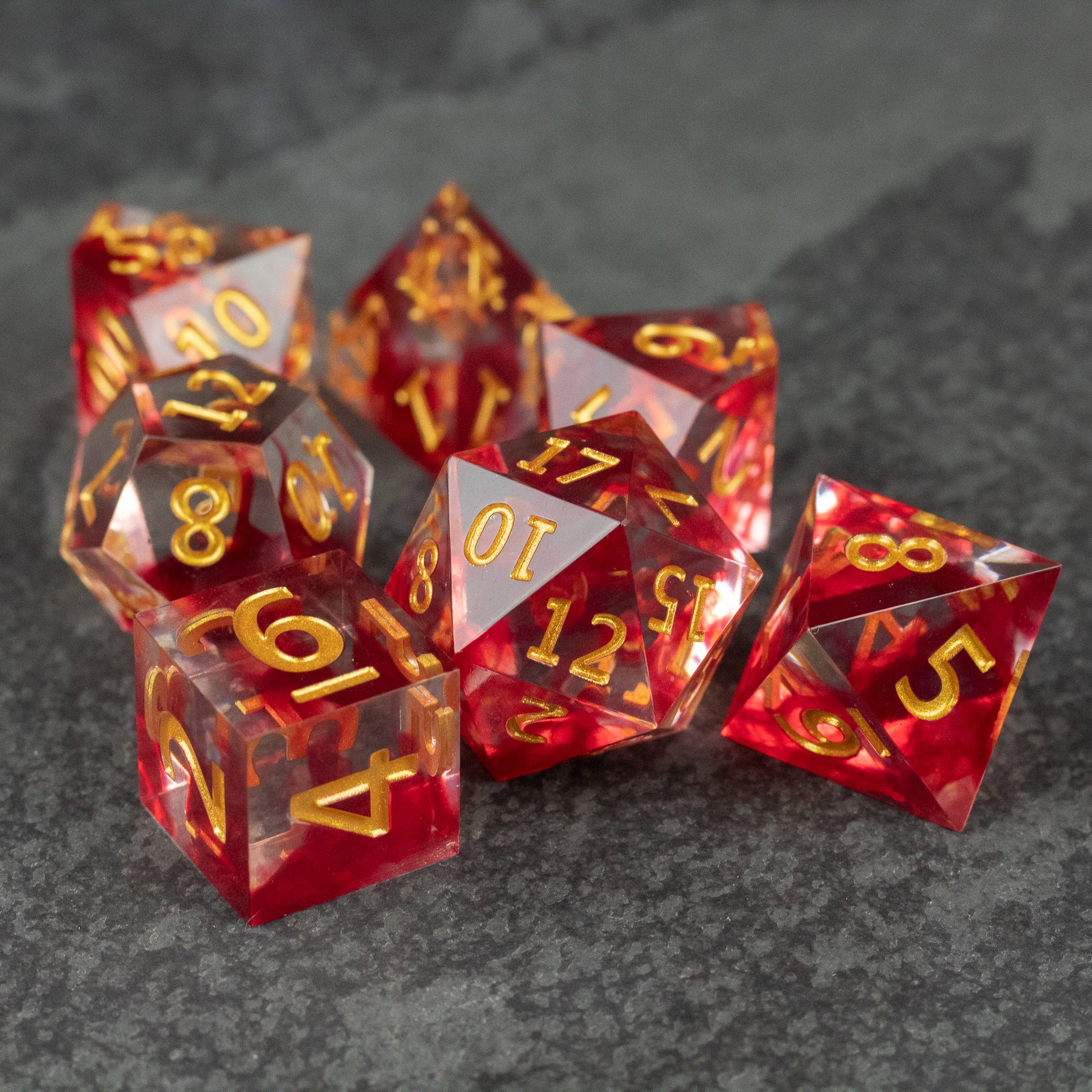 Blood Pact Dice Set - Red translucent sharp-edged polyhedral dice set with gold numbers on dark stone surface.