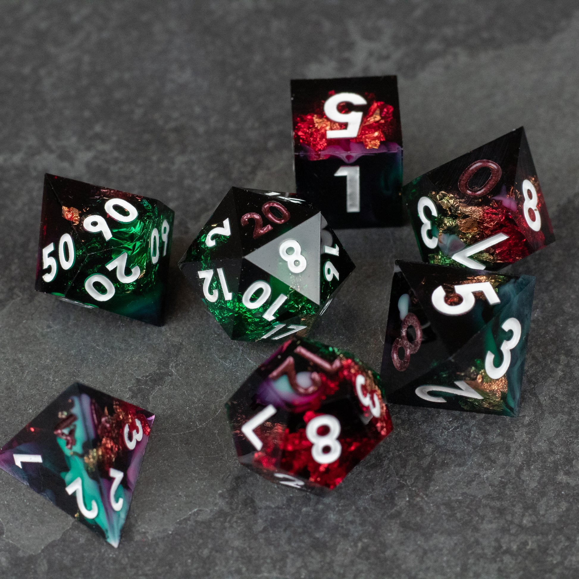 Chromatic Aberration Dice Set - Set of seven sharp-edged polyhedral dice with swirling red, green, and black colors and white numbering.
