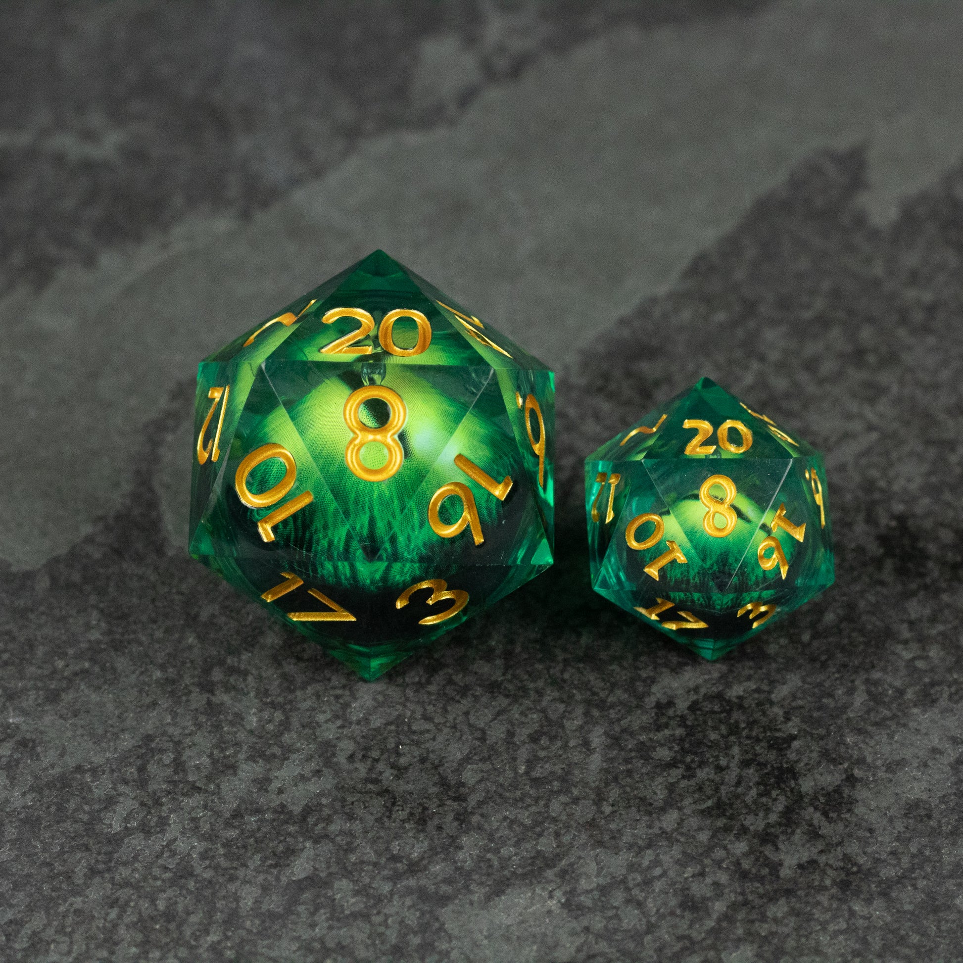 33mm Liquid Floating Eye - Purple - Two green translucent icosahedron dice with swirling liquid cores and yellow numbers on a dark textured surface.