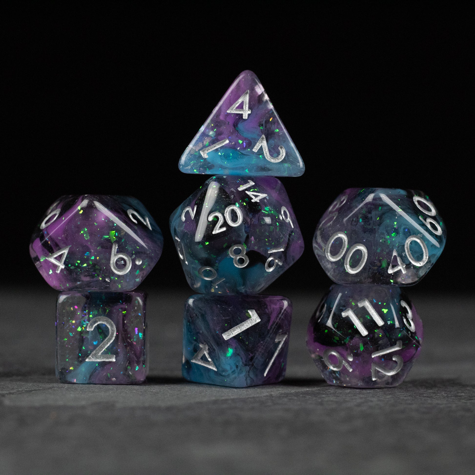 Purple and Black Spellweaver Dice Set - Seven purple and black speckled dice with white numbering, including d20, d12, d10, d8, d6, and d4 shapes.