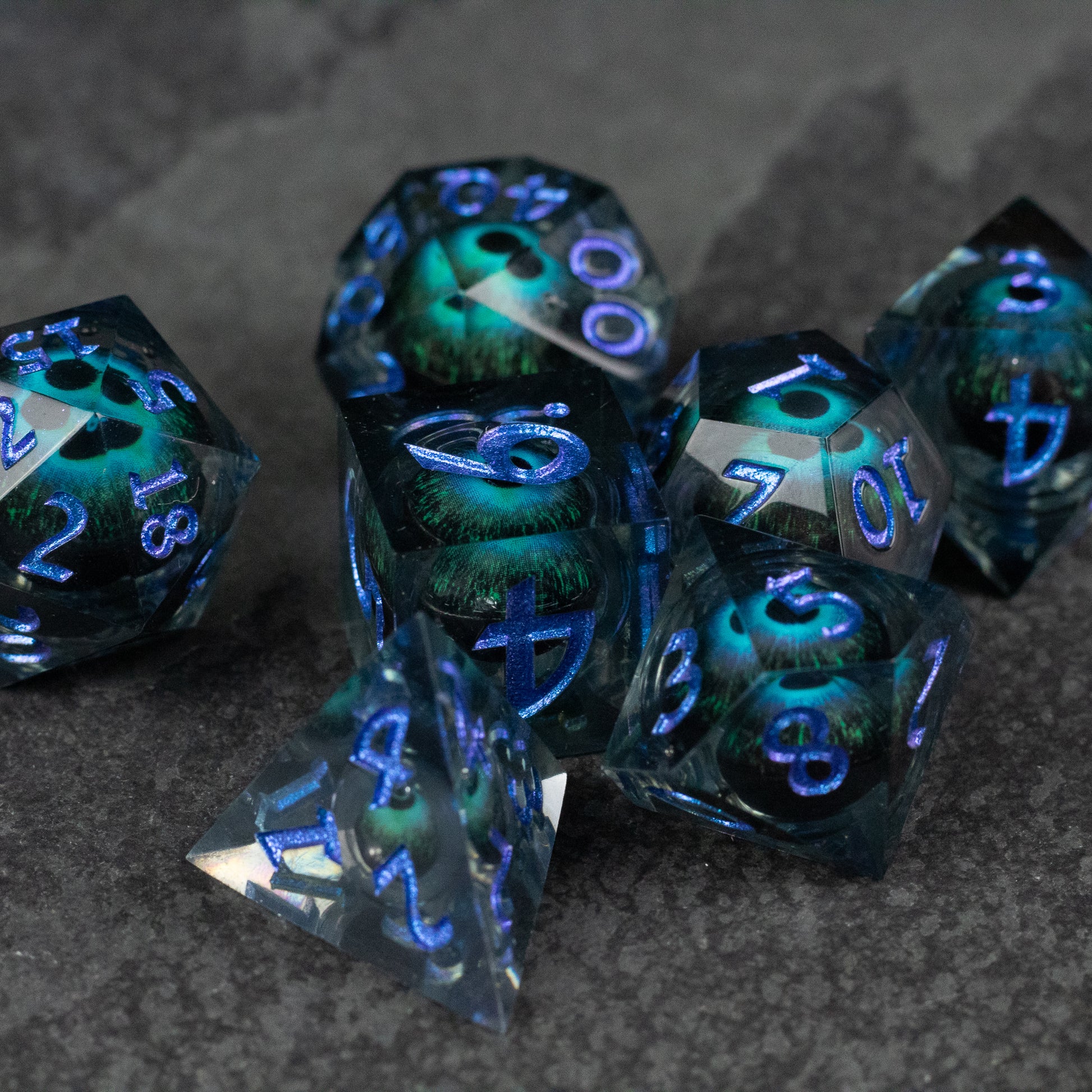 Blue Beholder's Eye Dice Set - Sharp-edged blue polyhedral dice set with glowing green liquid core and translucent faces.