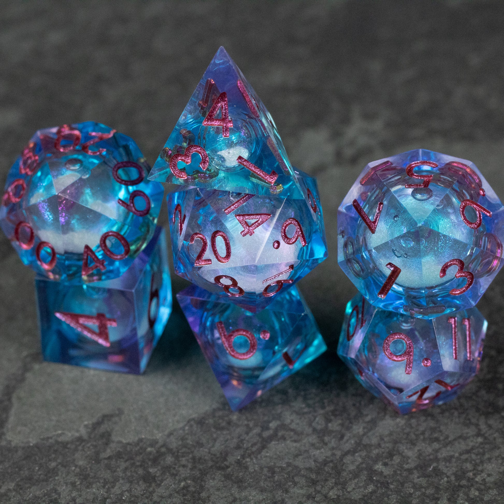 Crystallomancy Dice Set - Translucent blue polyhedral dice with sharp edges and red numbers, featuring a liquid core design.