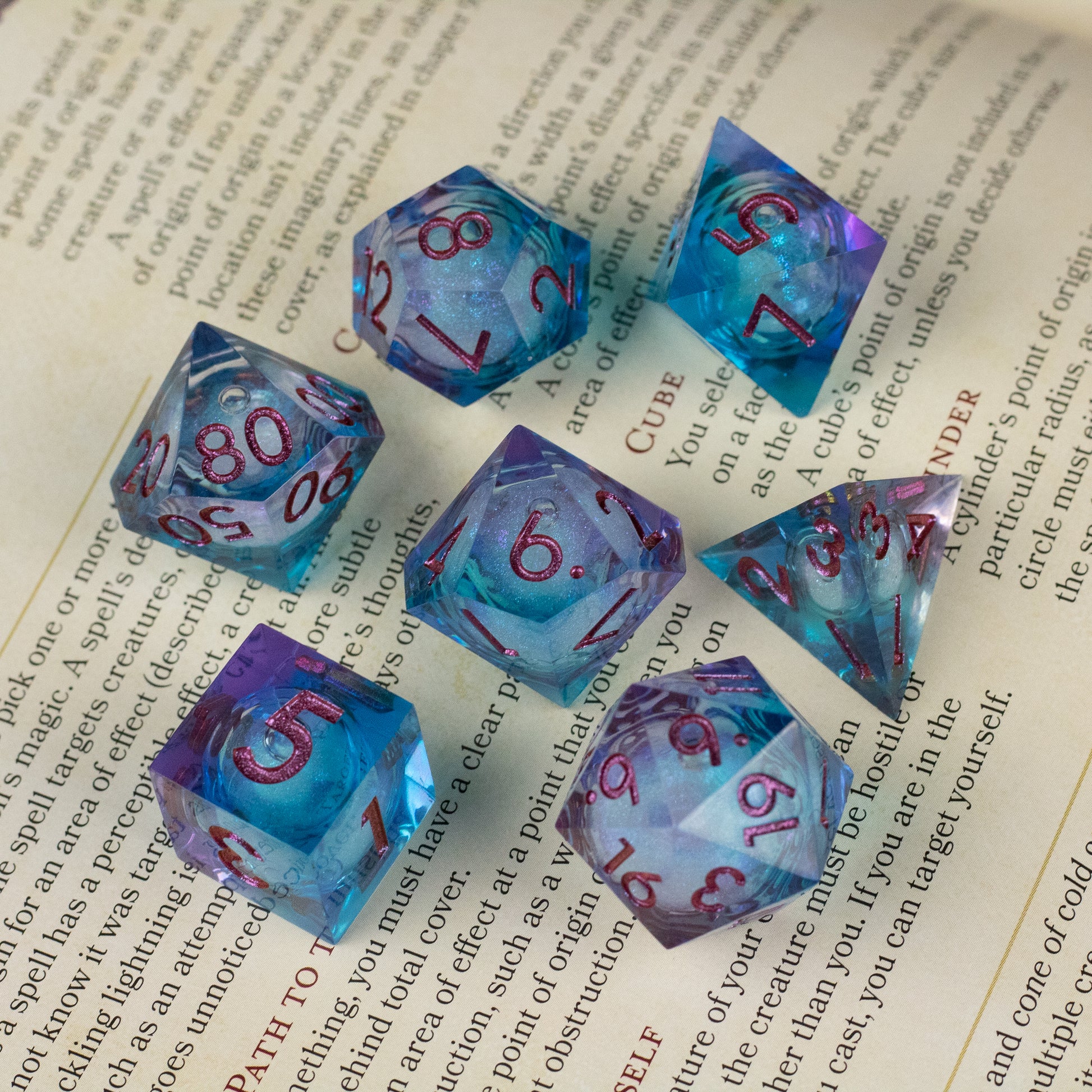 Crystallomancy Dice Set - Seven transparent blue polyhedral dice with swirling purple liquid core and sharp edges, red numbers, displayed on an open.