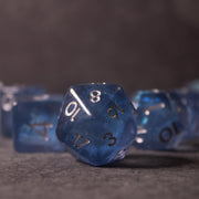 Glacier Ice Dice Set - Blue iridescent 20-sided dice with black numbers and inclusion details on gray surface.