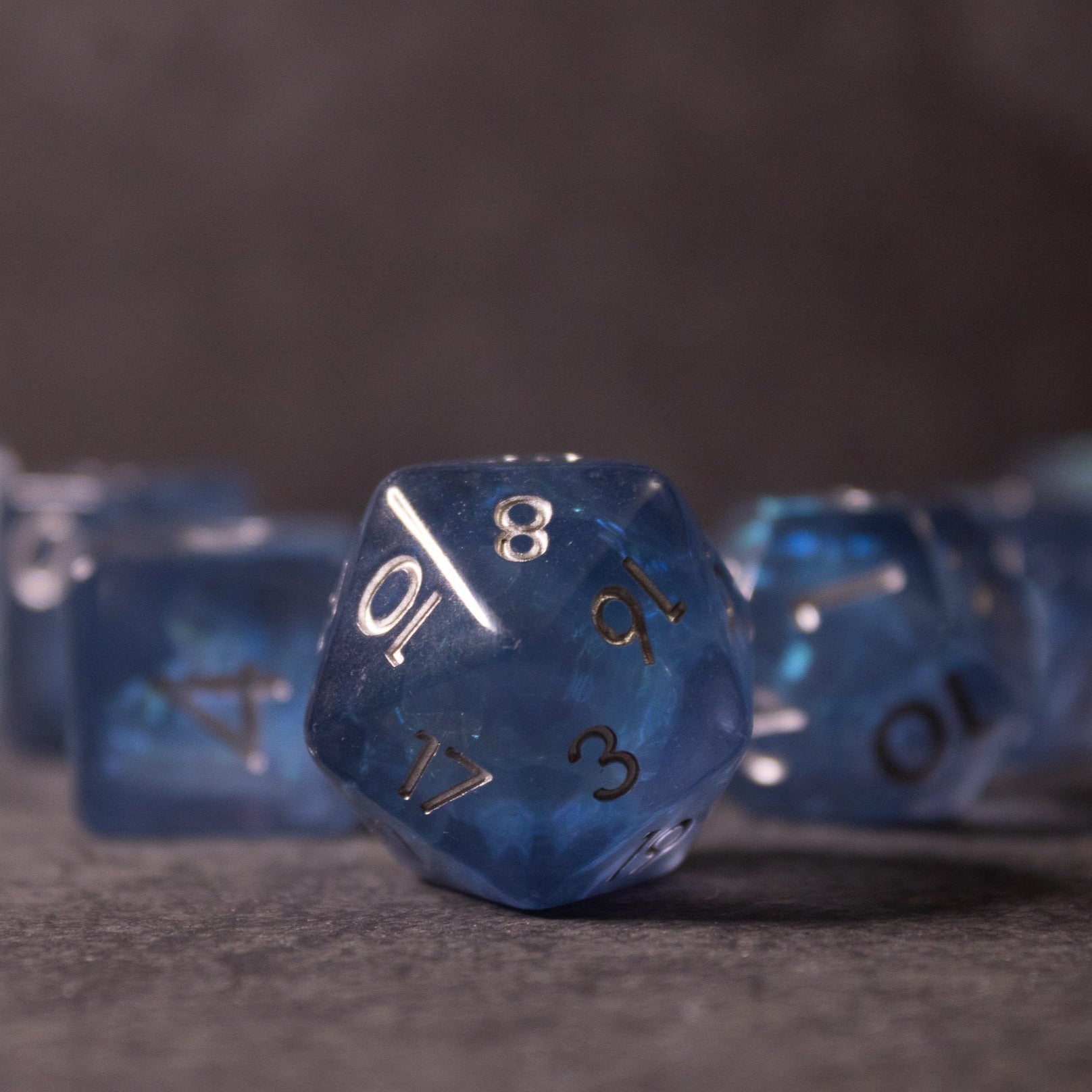 Glacier Ice Dice Set - Blue iridescent 20-sided dice with black numbers and inclusion details on gray surface.