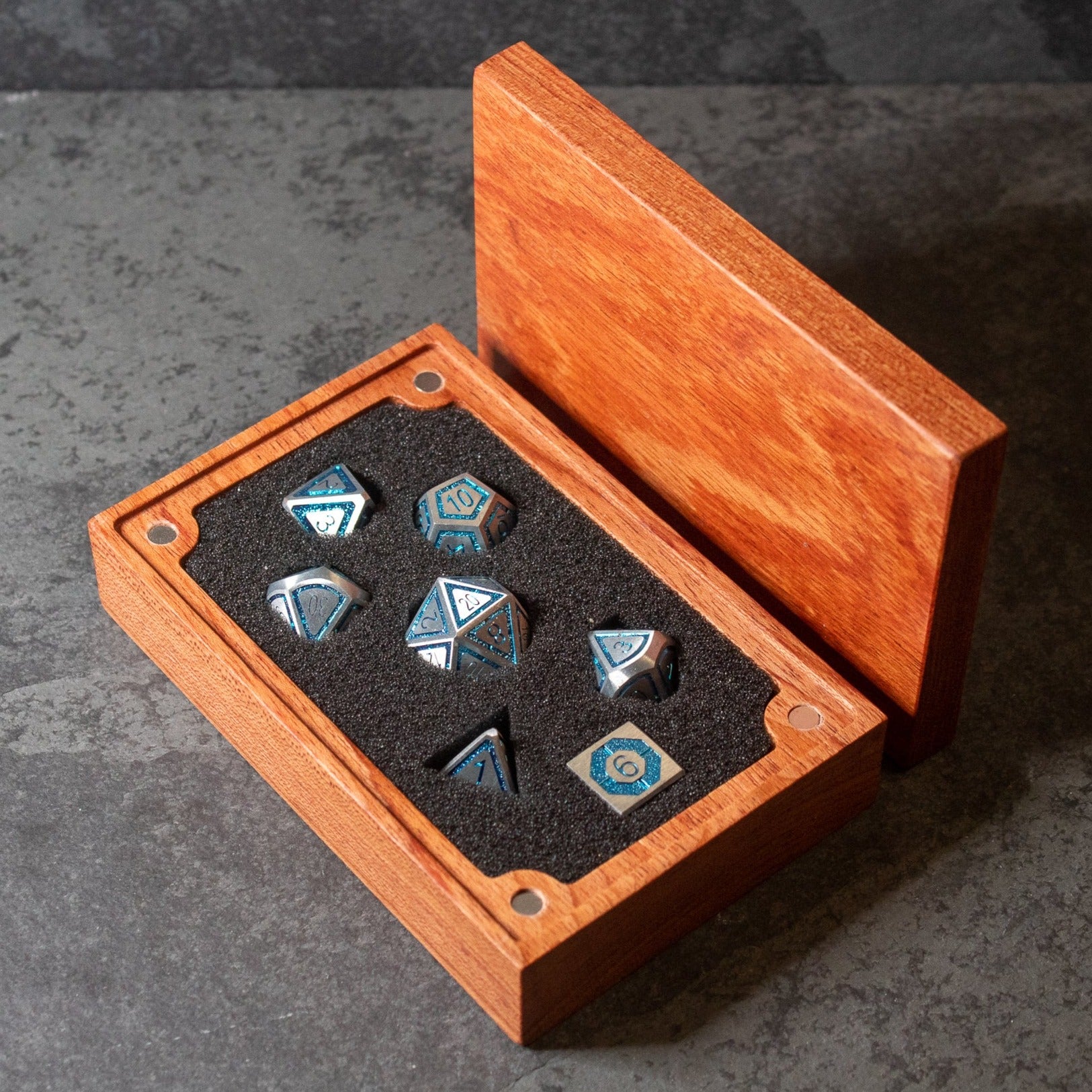 Cobalt Core Metal Dice Set - Set of seven blue metal dice with silver edges and numbers, displayed in a wooden box with black foam insert.