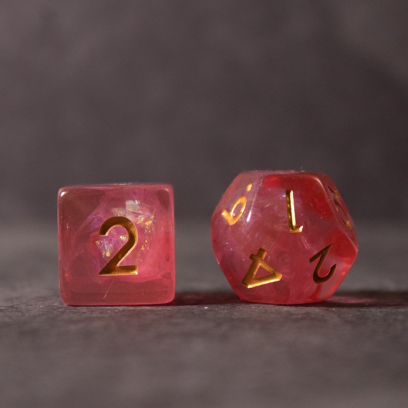 Pink Iridescent Dice Set - Translucent pink iridescent six-sided and twenty-sided dice with gold numbers.