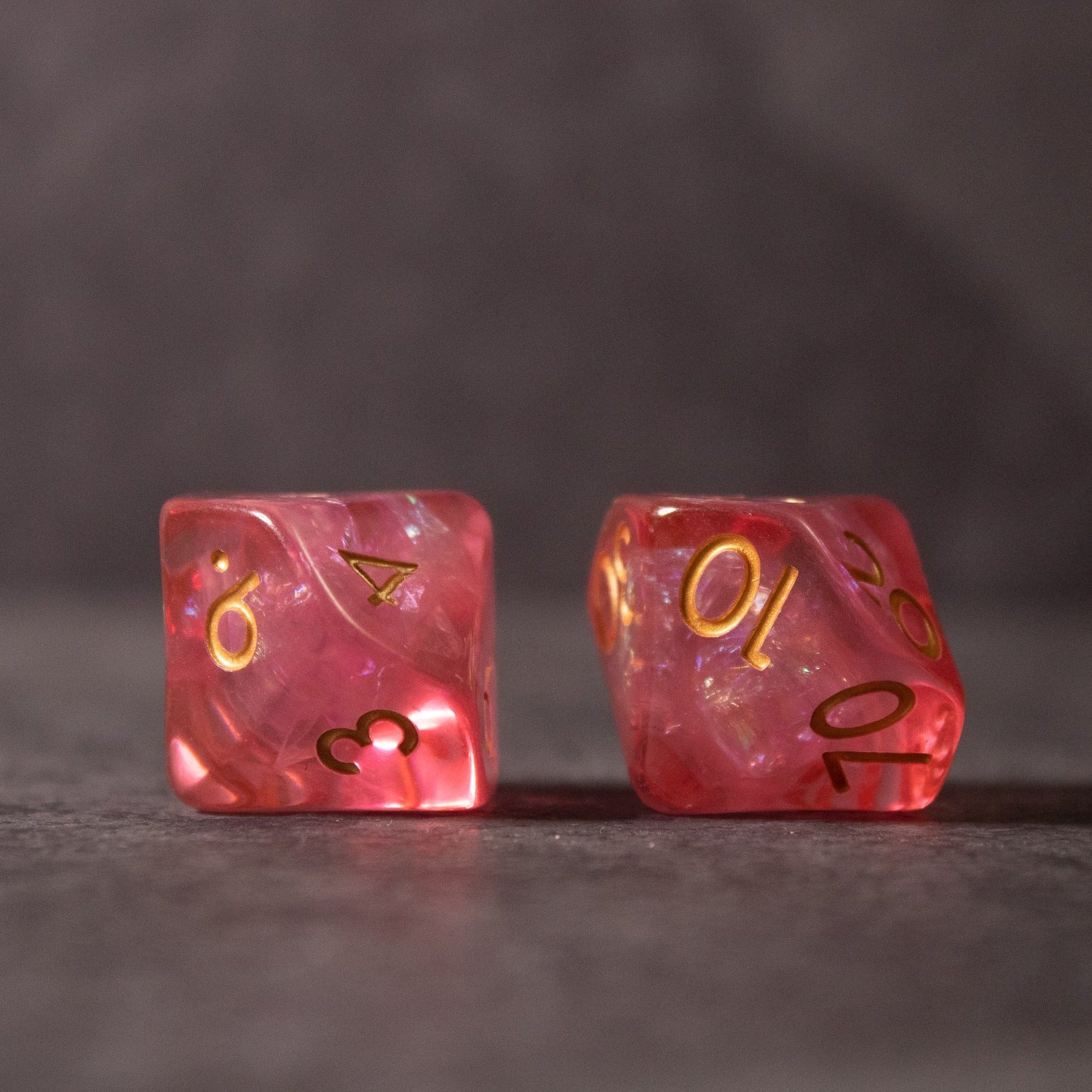 Pink Iridescent Dice Set - Two pink iridescent standard six-sided dice with gold numbers on a gray surface.
