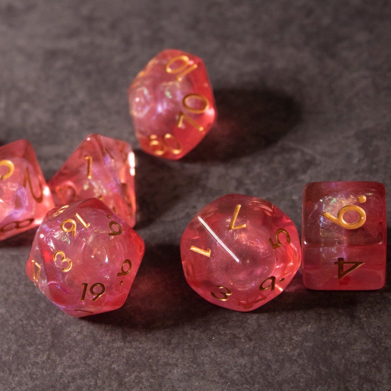 Pink Iridescent Dice Set - Set of pink iridescent polyhedral dice with gold numbering on a gray surface.