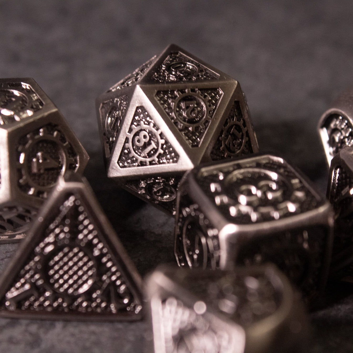 Metal Gear Dice Set - Set of metal dice with intricate engravings, including a d20, d12, d10, d8, d6, and d4 in dark silver finish.